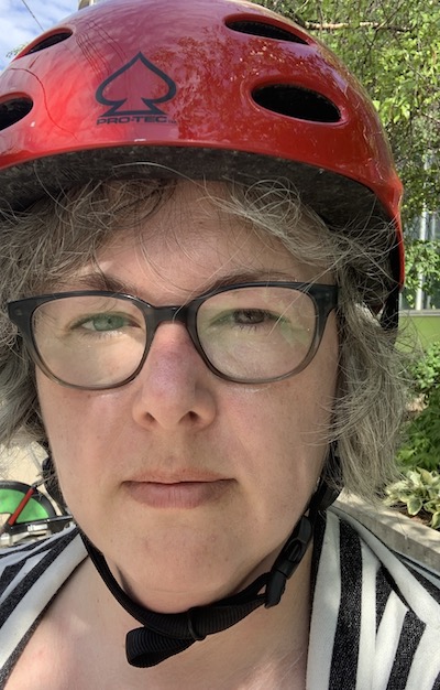 Amy, a white woman with salt-and-pepper hair, slightly sweaty, wearing a red bike helmet